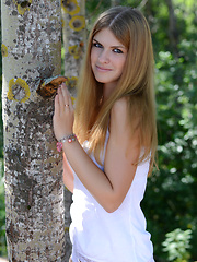 Admirable teen taking off clothes and posing naked in the shade of the trees near the sea.