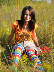 Wonderful teen beauty in long striped socks taking off her clothes outdoors in the field.